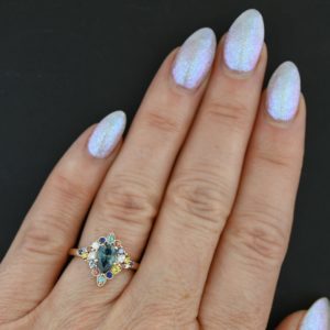 Oval vut montana sapphire engagement ring with muli-color gemstone halo, set in 14k rose gold. Handcrafted by custom jewelry designer Abby Sparks Jewelry.